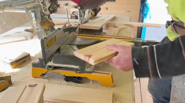 carpenter using power miter saw cutting wooden board in workshop.