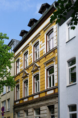 Fototapeta premium Historical yellow apartment building in Cologne Ehrenfeld with ornate window frames and peeling paint. A symbol of urban charm and renovation needs