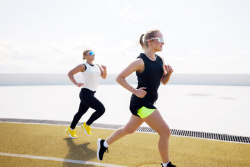 Fototapeta premium Two women jog together under a bright blue sky, enjoying a sunny day of exercise and friendship on an outdoor track