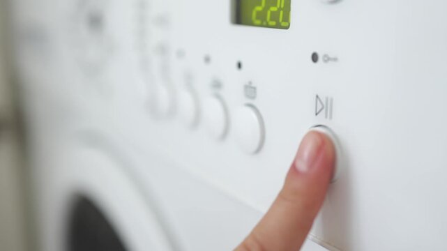 Finger pressing start button on washing machine before laundry cycle. Concept domestic chores and appliance operation.
