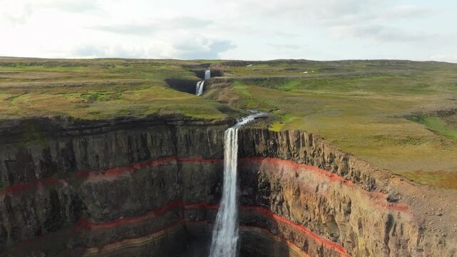 Aerial flight over the famous Hengifoss waterfall on a summer day in east Iceland. It has basaltic strata with thin, red layers of clay between the basaltic layers.
