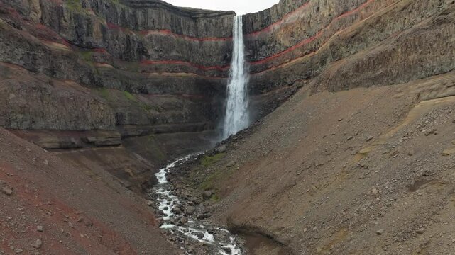 Aerial flight over the famous Hengifoss waterfall on a summer day in east Iceland. It has basaltic strata with thin, red layers of clay between the basaltic layers.