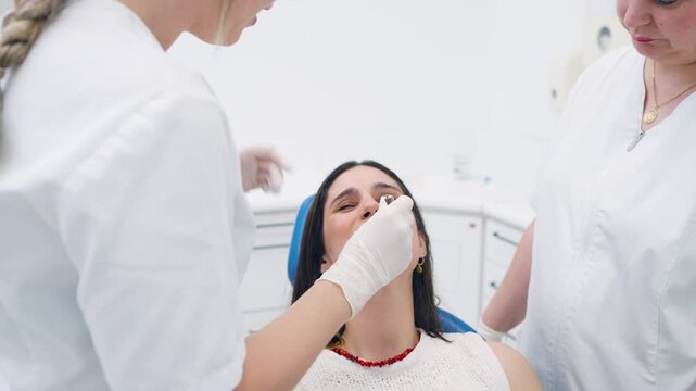 Professional dentist and assistant taking a dental impression from a female patient in a modern clinic. The team is making a mold of teeth