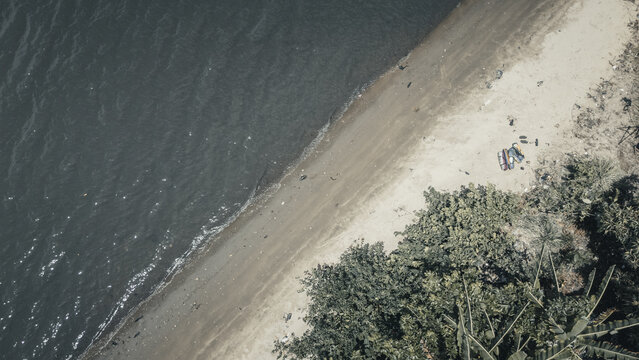 Aerial view of the tranquil shoreline where dark rippling water meets a sandy beach bordered by lush tropical greenery Badagry, Lagos, Nigeria.