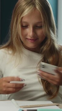 Focused Caucasian little girl child using mobile phone writing test in classroom cheating AI assistant kid schoolgirl student dishonest study pupil teenager exam task internet education problem school