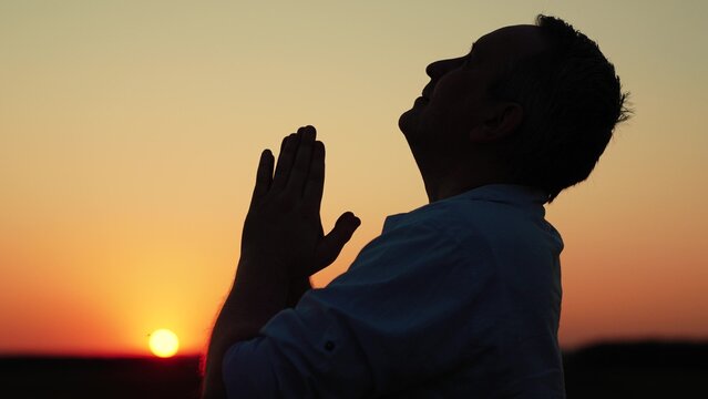 Christian man praying at dawn, close-up. Man confesses. Faith in God. Man prays family children against backdrop sky sun. Relaxation meditation nature. Apologizing. Hope. People religion. Silhouette