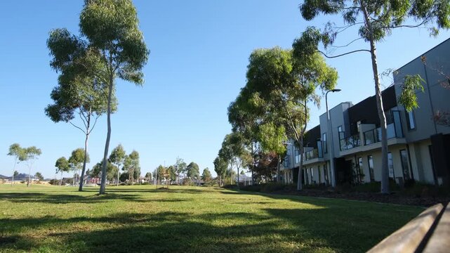Wide view of a green public parkland with native eucalyptus trees bordering a row of modern two-story townhouses in Melbourne Australia. Interface between residential density and green space.