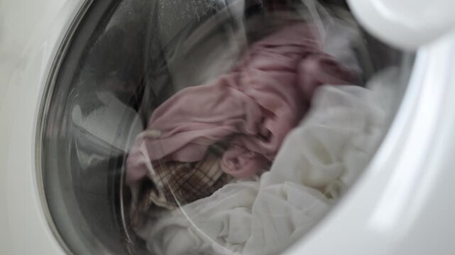Washing machine drum filled with white and pink laundry spinning rapidly, showcasing the continuous motion of clothes during the washing cycle in a modern home setting