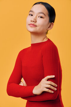 Young woman wearing red sweater standing with crossed arms looking confidently at camera on bright yellow background. Portrait with natural expression and casual pose in studio.