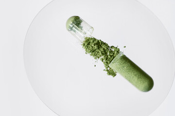 Open capsule spilling green powder on white surface, representing natural health © colnihko