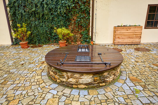 Wooden-covered well in cobblestone courtyard with plants and ivy on wall