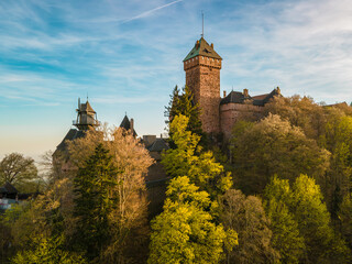 Castle Haut-Koenigsbourg, Alsace, France - April 10, 2026 - Tall tower rising above treetops with dramatic sky backdrop, crisp masonry details, warm evening light highlighting turret edges © Oksana