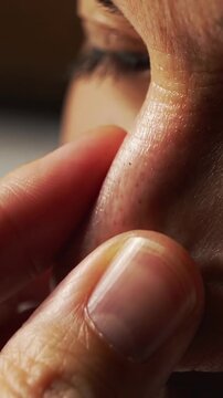 Vertical video: Approaching man's thumb and index fingers pinching nostril at home, checking skin