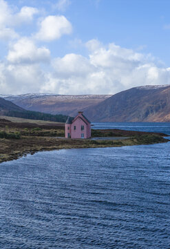 Aerial view of The Pink House on the shore of Loch Glass surrounded by rolling hills and blue water under a cloudy sky Dingwall, Scotland, United Kingdom.