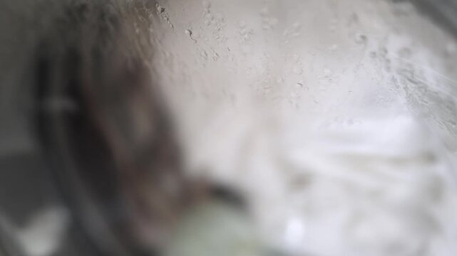 Laundry being washed inside a washing machine drum with water and detergent creating bubbles and foam, showcasing the cleaning process in action