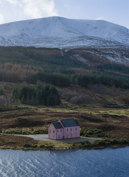 Aerial view of The Pink House on the shore of Loch Glass with a snow-capped mountain and dense pine forest in the background Dingwall, Scotland, United Kingdom.