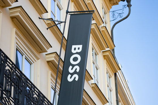 Vertical black banner displaying the logo "BOSS" hanging from a decorative bracket on a building facade with windows and architectural details visible