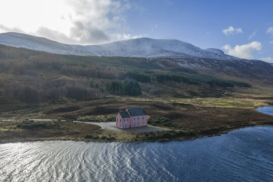 Aerial view of The Pink House on the shore of Loch Glass with snow-capped mountains and rugged terrain in Dingwall, Scotland, United Kingdom.