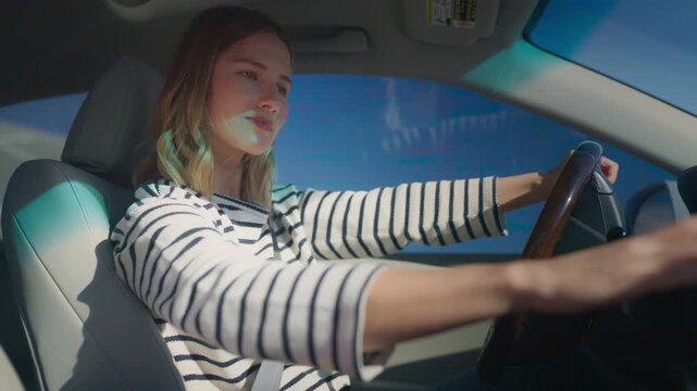 Young pretty woman driving car, switching gears while holding steering wheel. Focused expression of beautiful female driver learning to drive auto. Nice day and blue clear sky.