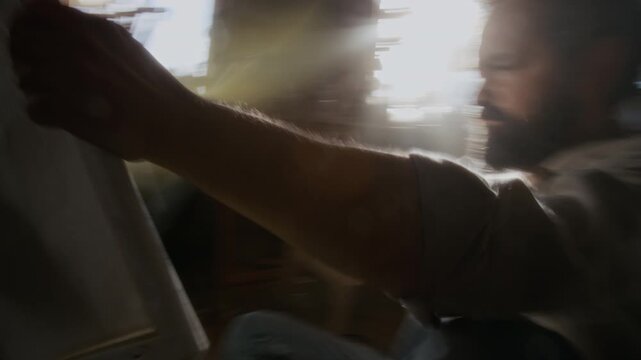 Handheld camera shot with motion blur of desperate artist ripping canvas while experiencing emotional burnout and creative struggle in cluttered studio bathed in bright sunlight