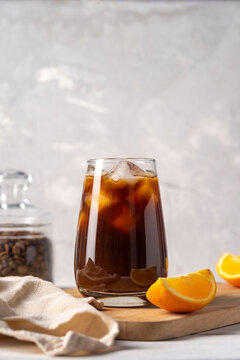 Coffee with orange juice bumble in a tall glass with ice on a light background with coffee beans, fruits and morning shadows