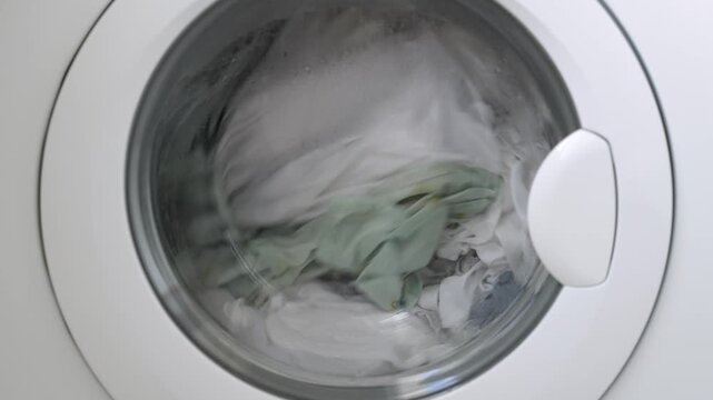 Washing machine drum filled with white and light green laundry, water and bubbles visible, showcasing the washing process in a modern appliance