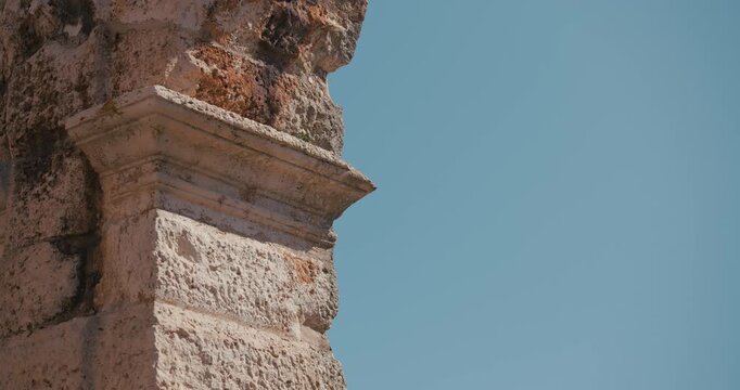 Close up view of a weathered stone wall detail of the ancient Pula Arena Roman amphitheater against a clear blue sky in Pula Croatia.