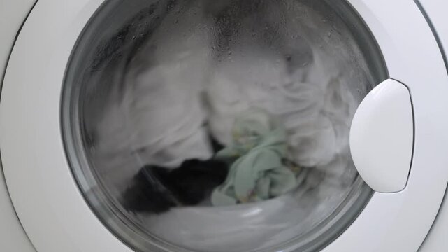 Washing machine drum filled with white laundry, showing a close-up view of wet clothes in motion, with water and steam visible through the glass door