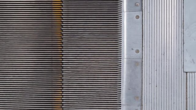 Overhead view of moving escalator steps connecting with metal landing plate. Close-up of escalator in subway station or mall. Lines, patterns, durable metal surfaces of public transit infrastructure
