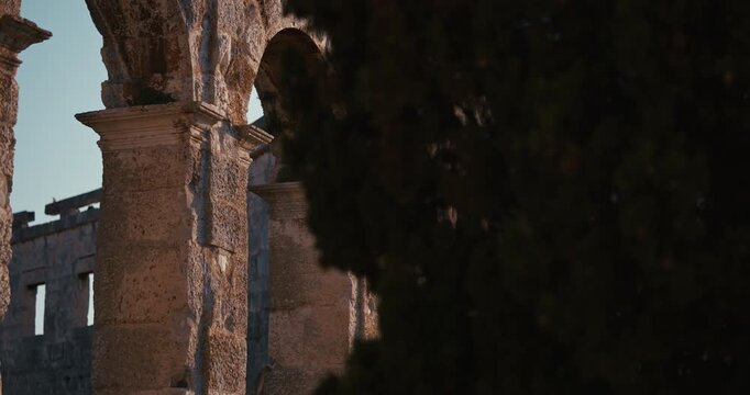 Close view of the stone arches and columns of the ancient Pula Arena partially framed by dark tree branches in Pula Croatia.