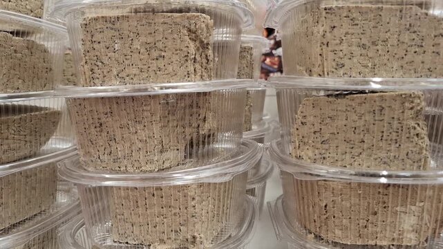 Close-up view of fresh sunflower halva blocks packed in clear plastic containers. The delicious oriental sweet dessert with poppy seed inclusions is stacked in neat rows on a store or market shelf