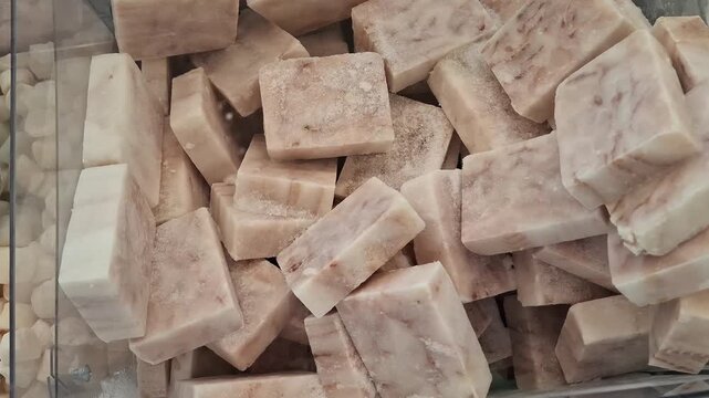 Frozen fish fillet cubes covered with light frost in store display freezer. Rectangular pieces show a pink and white marbled texture. Pile of seafood briquettes. Pressed blocks of frozen fish meat