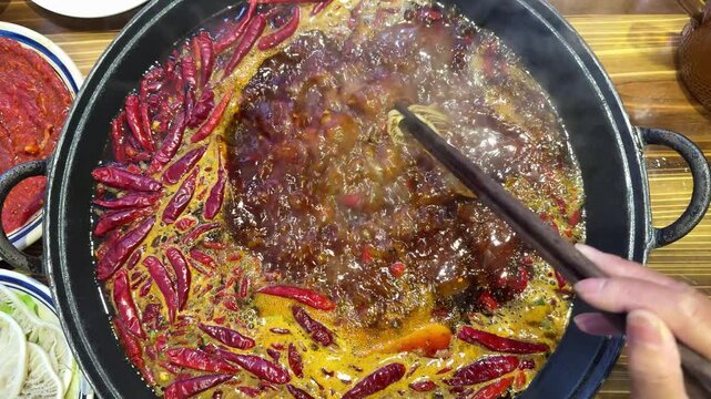 Close up shot of spicy red oil boiling with dried chilies in a traditional Sichuan hotpot at 30fps slow motion.