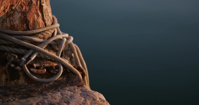 Wrapped rope on a rusted mooring bollard beside calm water in low sunlight in Pula Croatia.