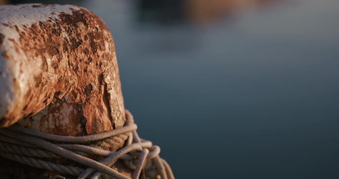 Close up of a rusted mooring bollard with wrapped cable beside calm water in low sunlight in Pula Croatia.