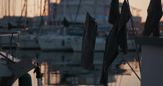 Dark fabric hanging on poles near docked boats in a marina during evening light.
