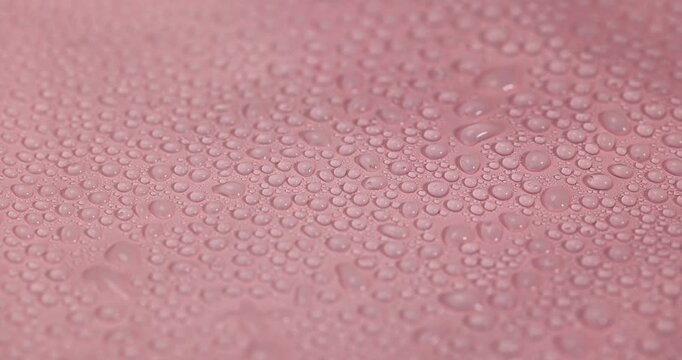 A film with moisture droplets, a thin pink film with a wet surface and lots of clear water droplets under artificial lighting with an authentic look and organic texture.