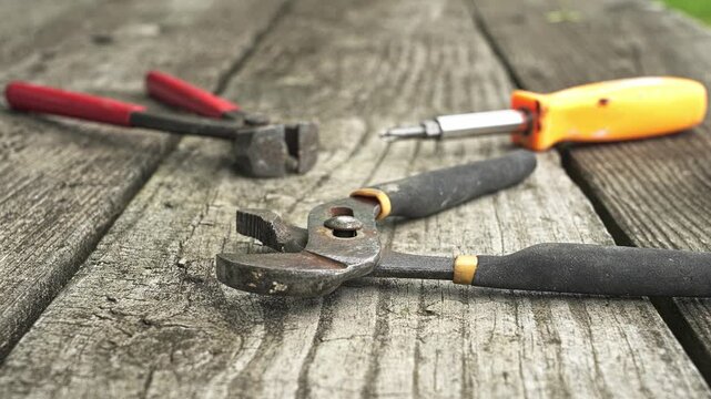 Old, used pliers and a screwdriver lying on a rustic wooden plank surface. Handyman or carpenter tools for repair and maintenance work