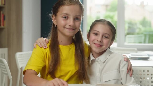 Happy two Caucasian little girl child hugging friend classroom cute friendship kids schoolgirls students pupil sisters children cuddle embrace smiling looking camera education bonding together school