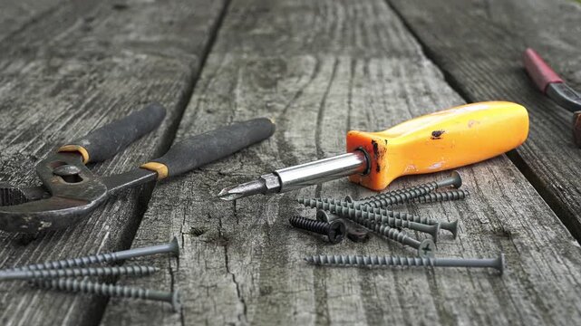 Handyman tools and screws resting on an old, weathered wooden table. Pliers, a screwdriver, and different types of screws are visible