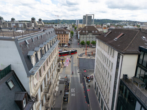 Aerial view of urban architecture, a red bus crossing a street, and distant hills under a cloudy sky in Biel Bienne, Canton of Bern, Switzerland.