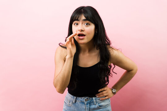 Young lady sharing juicy gossip or reacting to shocking news in hushed tones against a vibrant pink backdrop