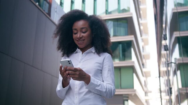 Successful African American business woman walking downtown using mobile phone smartphone outdoors in city female businesswoman girl entrepreneur worker ebusiness online chat cellphone gadget outside