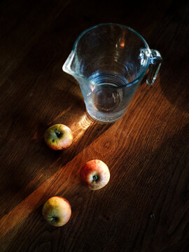 Still life of a glass jug and three apples on a wooden table