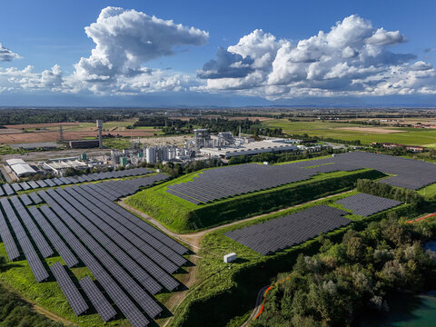 Aerial view of a large solar panel farm and industrial facility under a dramatic cloudy sky in Crescentino, Piedmont, Italy.