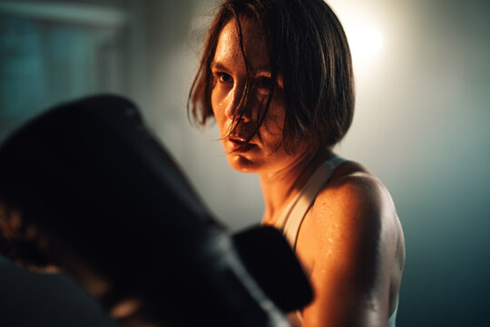 Female boxer training hard, sweating, focusing on intense workout, building strength and determination in gym