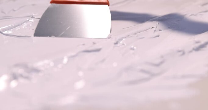 Woman in protective gloves applying white plaster with putty knife onto grey surface, closeup. Camera tracking