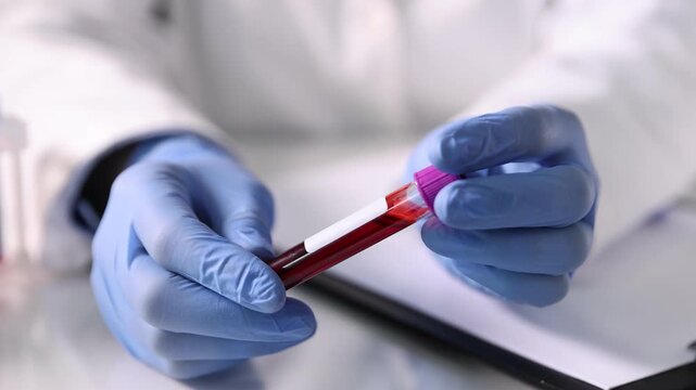 Laboratory worker with blood sample in test tube at table indoors, closeup