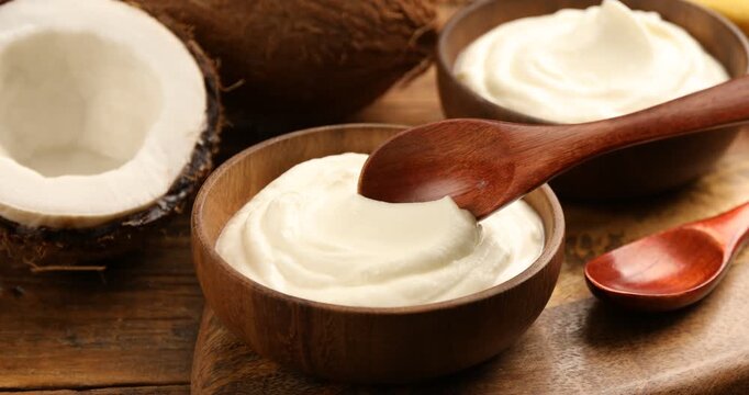 Woman with tasty coconut yogurt and nuts at wooden table, closeup