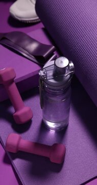 Sports equipment and water bottle on purple background, closeup. Camera moving